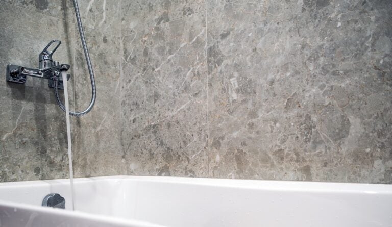 Water running from modern chrome faucet into white bathtub