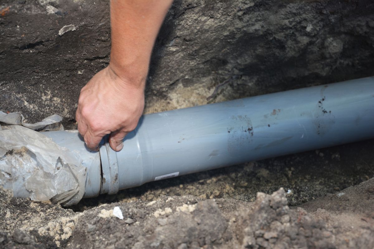 Contractor installing house sewer pipe in the ground trench
