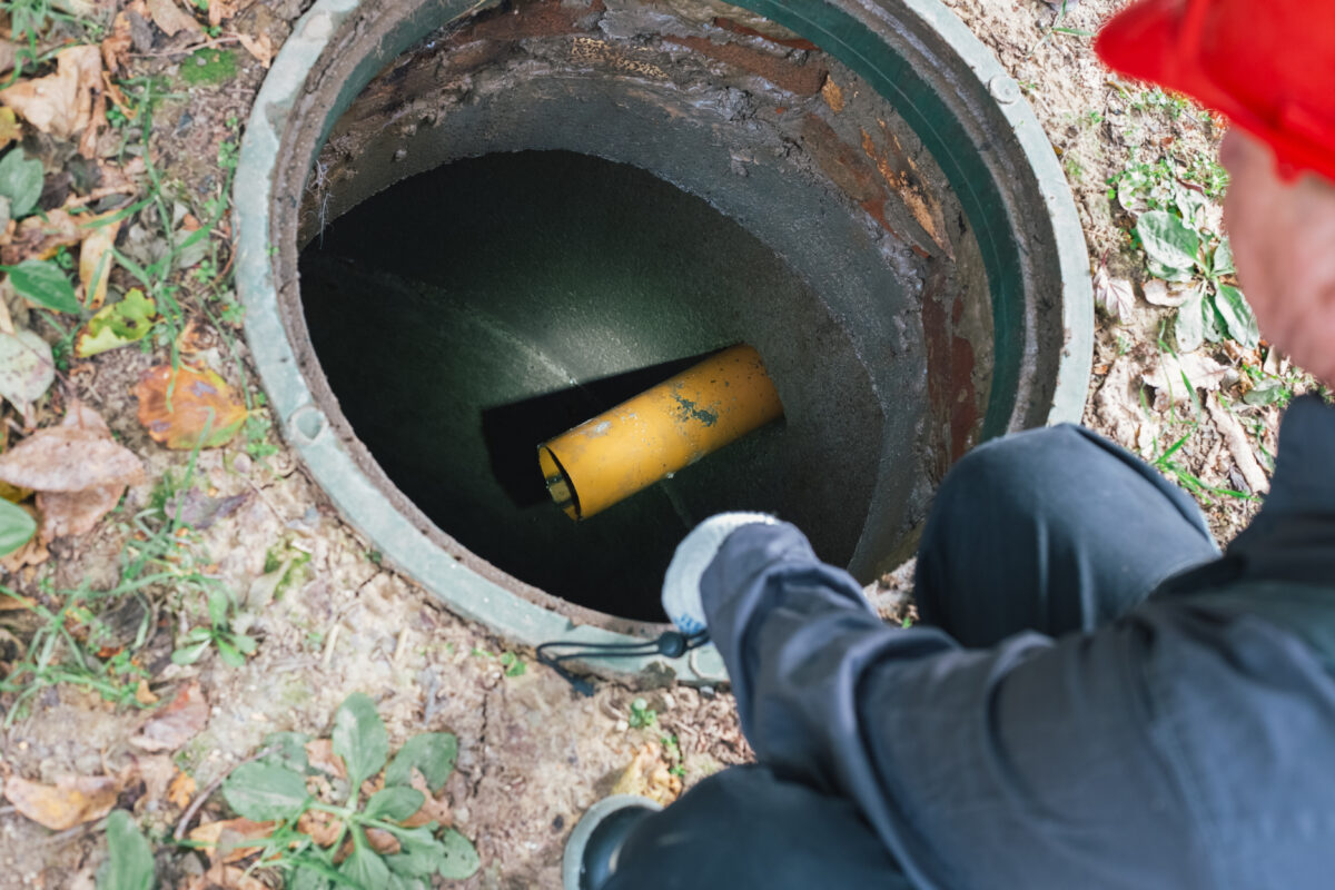 A worker with a flashlight inspects an open sewer manhole. Septic tank maintenance, sewage pumping.