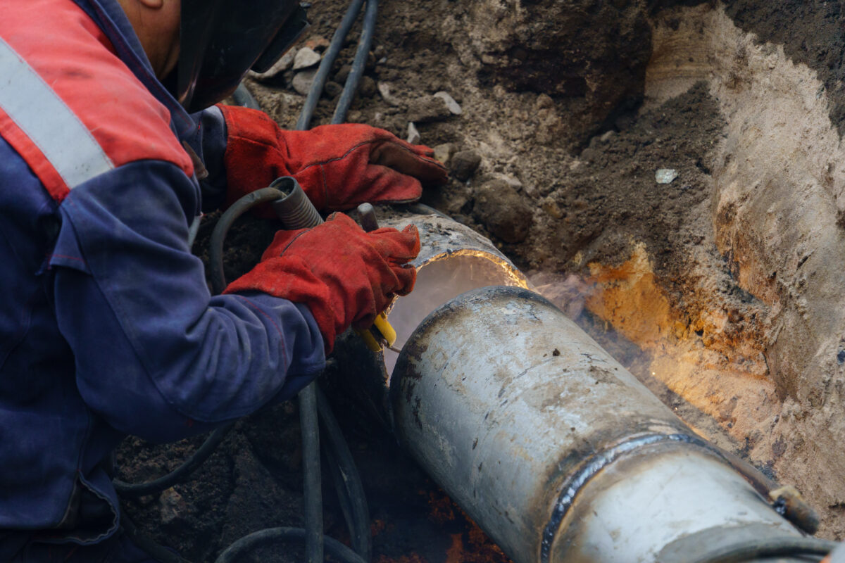 septic vs sewer Plumber standing in pit is engaged in elimination of communal accident outdoors. Utility worker fixing broken water main. Welding work to replace rotten elements of water pipe. Sewerage pipe repair